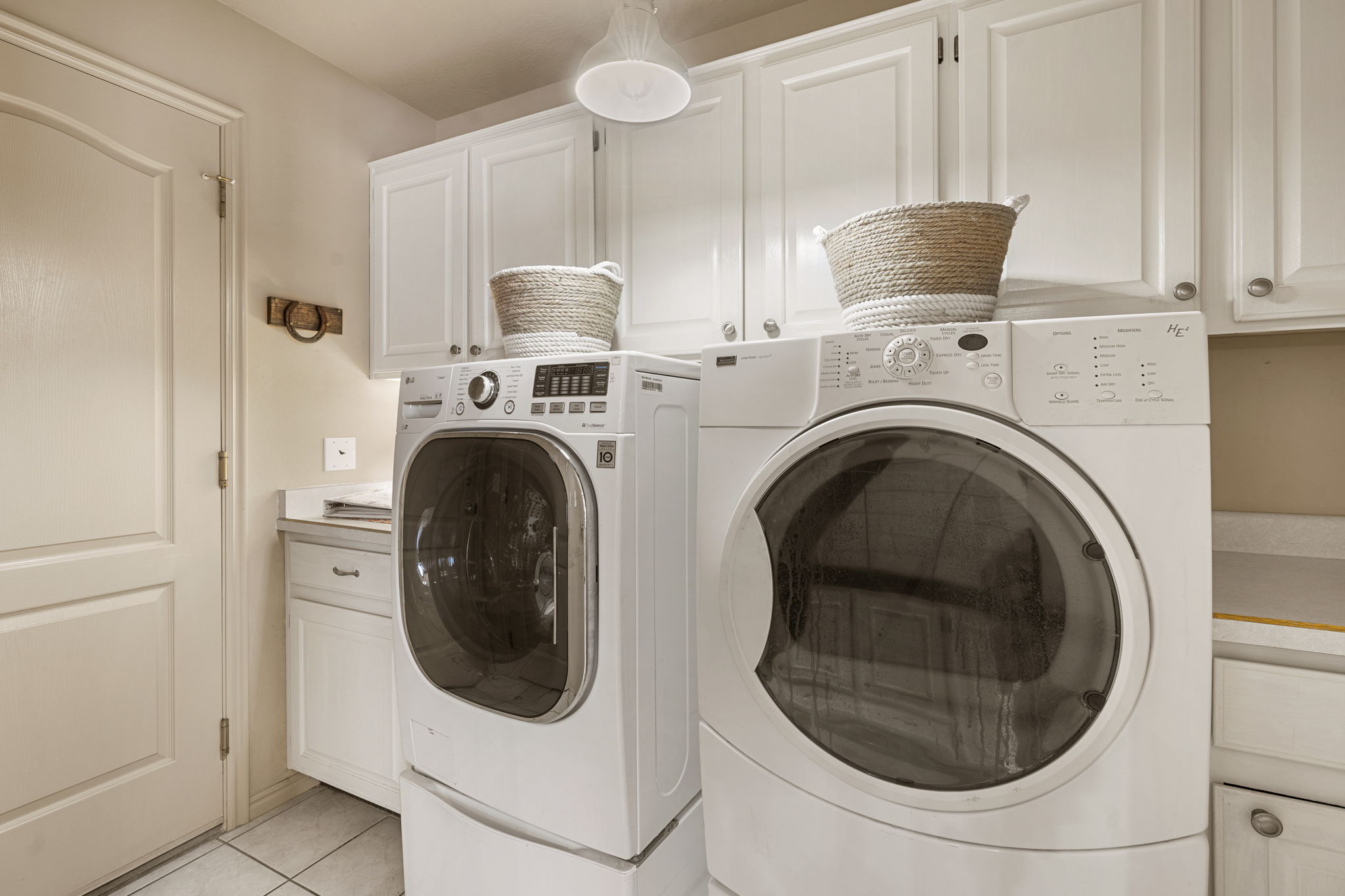 Laundry area featuring white cabinetry with brushed nickel hardware, light-toned countertops, and tile flooring