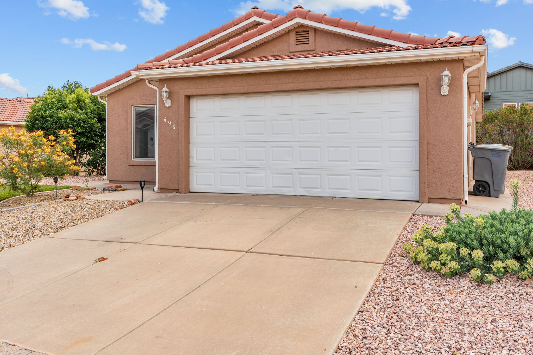 Stucco exterior featuring a two-car garage with panel door, concrete driveway, terracotta roof tiles, and exterior sconce lighting
