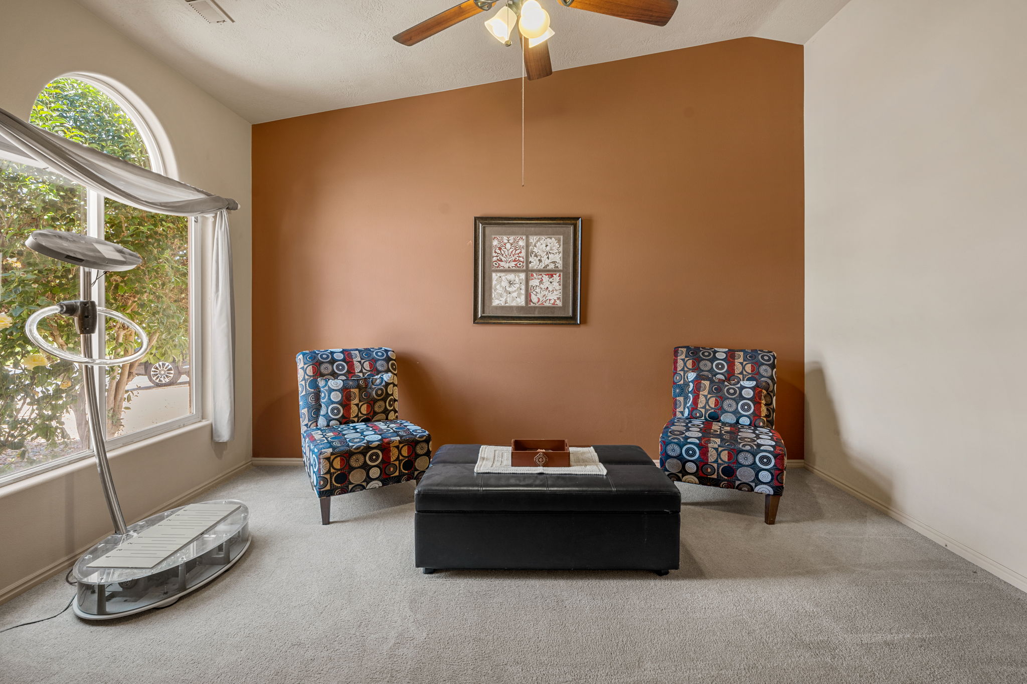 Room featuring a vaulted ceiling with a ceiling fan light fixture, arched window, and light-toned carpeting