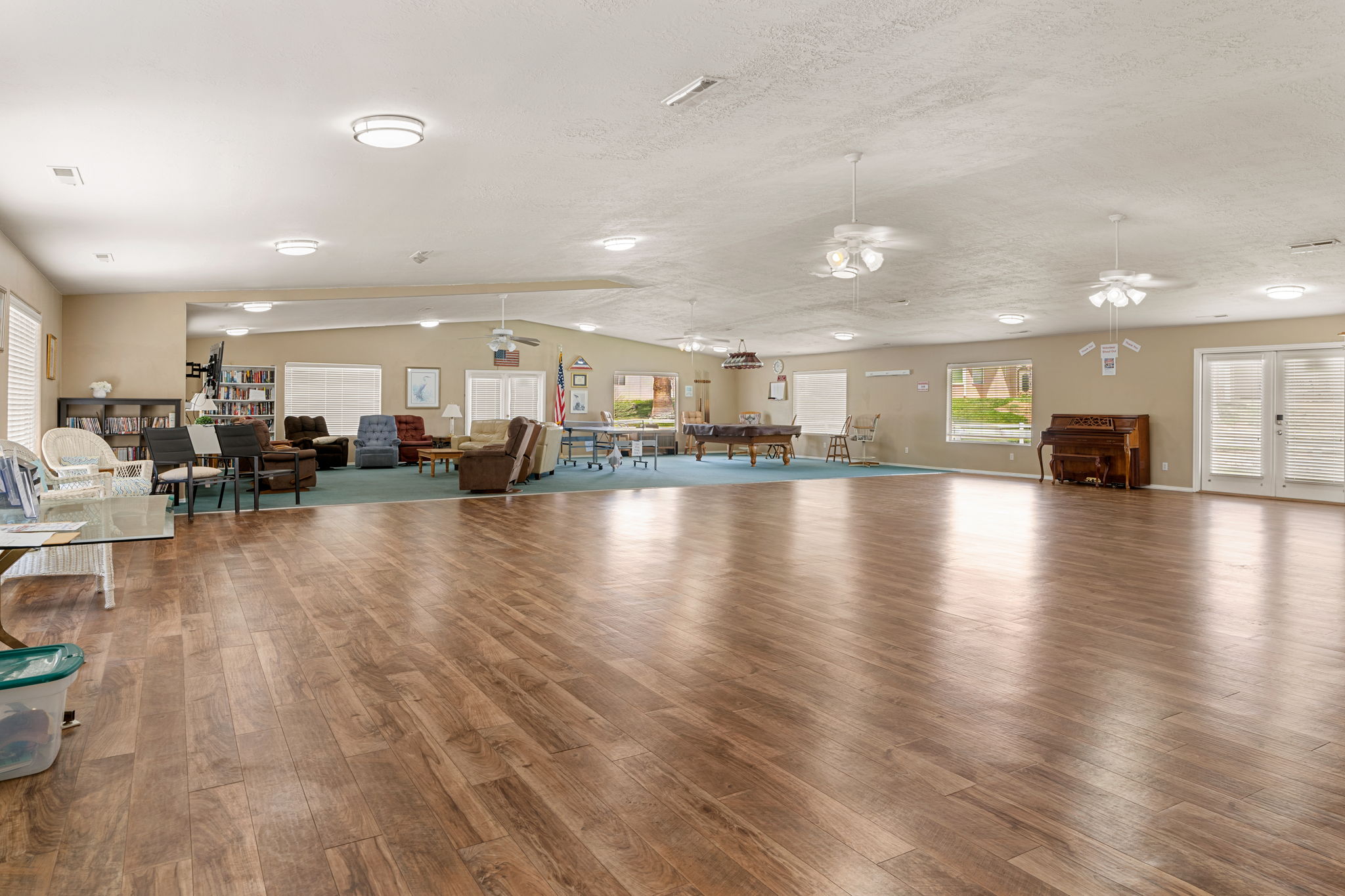 Expansive common area featuring wood-finish flooring, recessed lighting, ceiling fans, and multiple windows