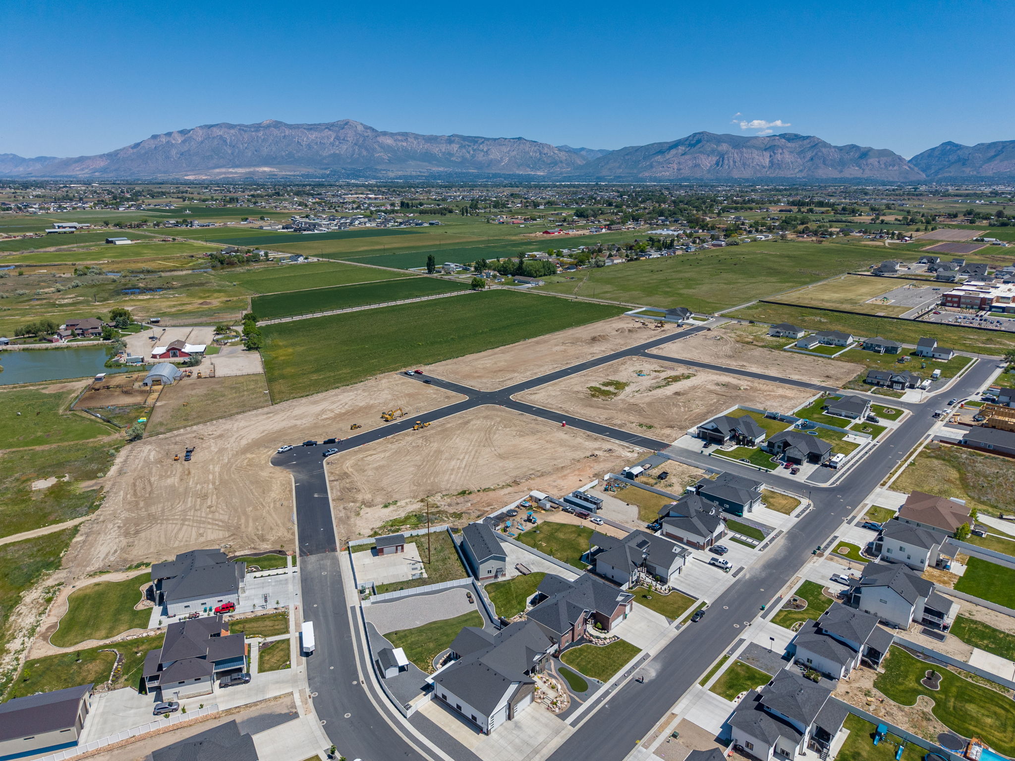 Developing residential area with mountain backdrop, established road infrastructure, and surrounding agricultural land