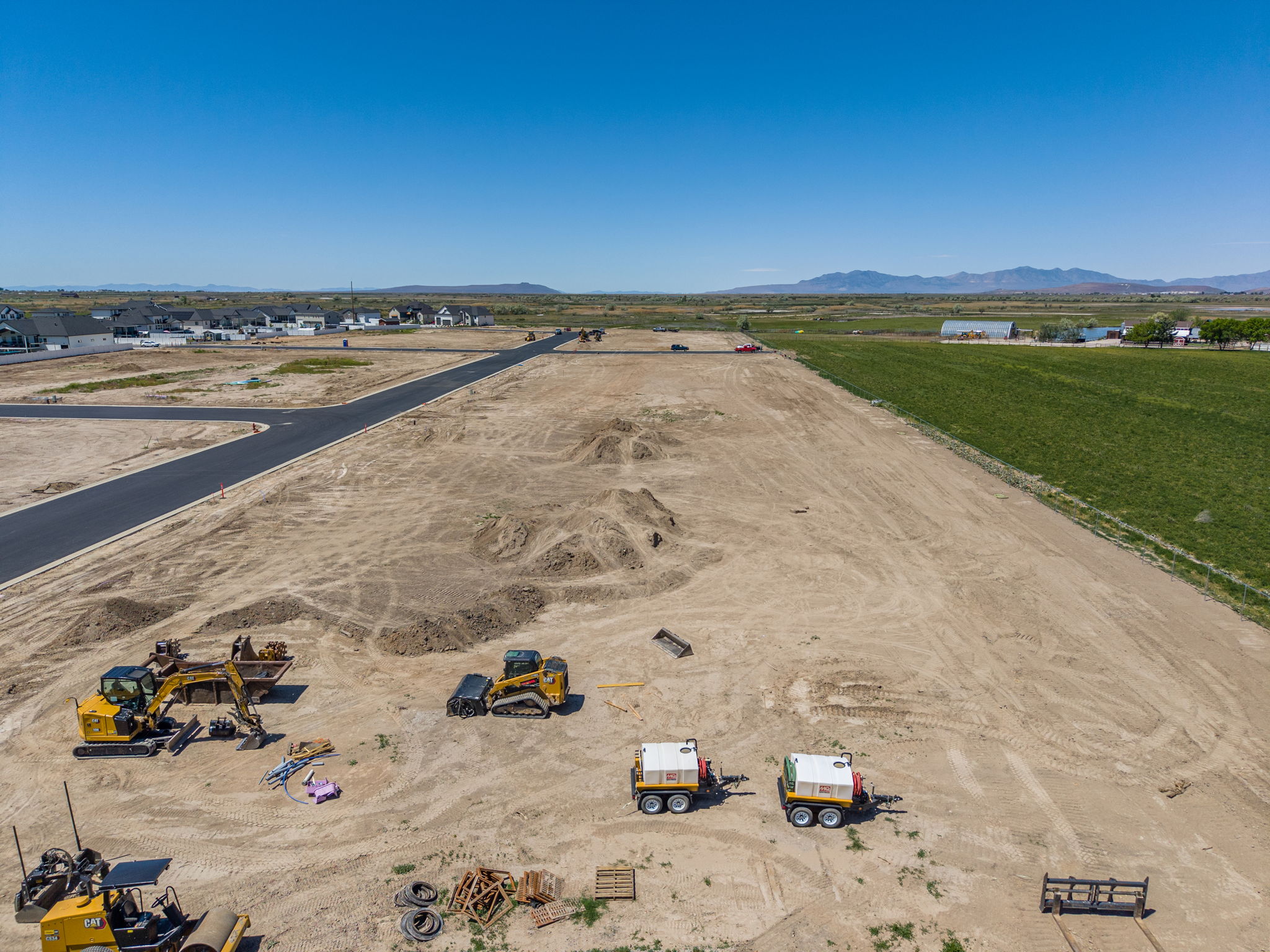 Expansive undeveloped land featuring a newly paved road, surrounding agricultural fields, and distant mountain ranges
