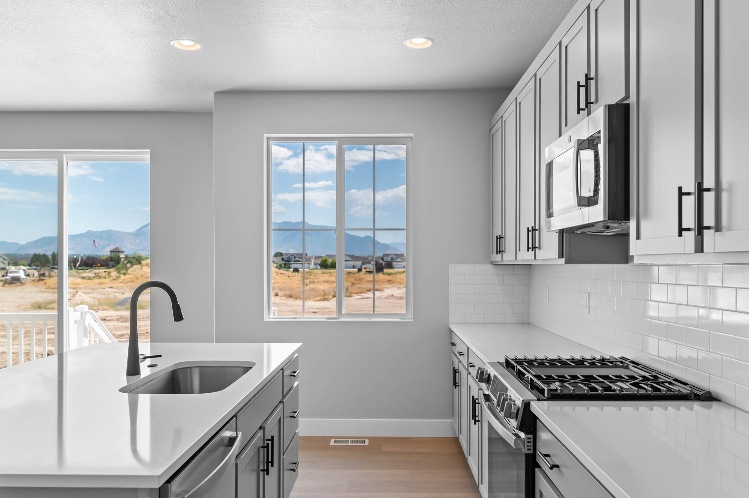 Modern kitchen featuring a stainless steel sink, black gooseneck faucet, light grey cabinetry, white countertops, and a subway tile backsplash