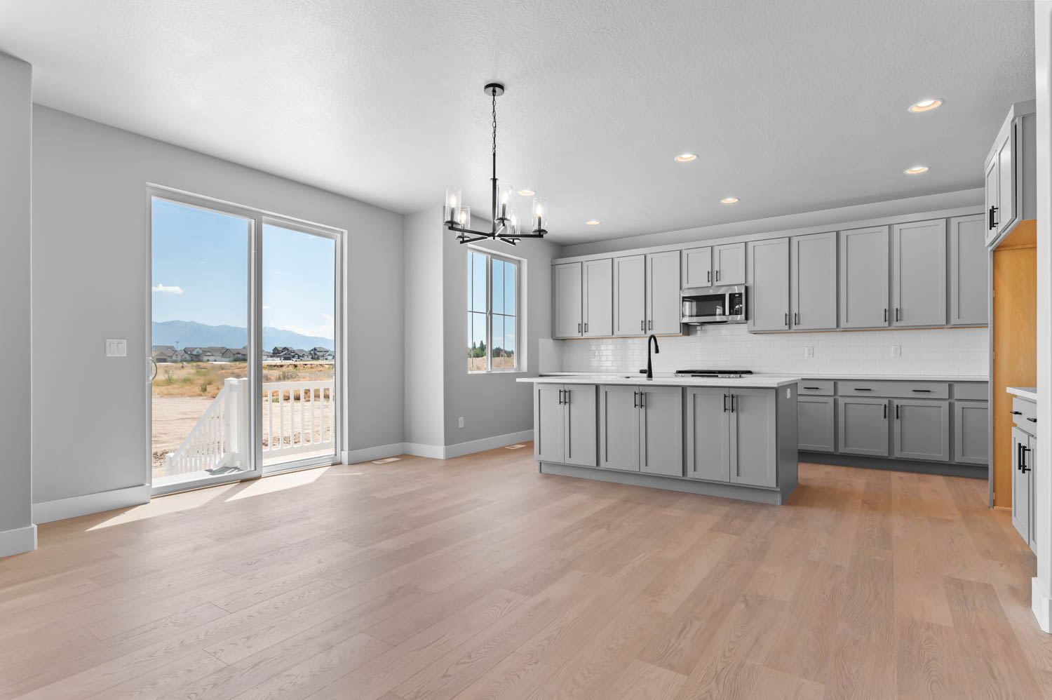 Open-concept kitchen and dining area featuring light wood-finish flooring, grey cabinetry, white countertops, and stainless steel appliances