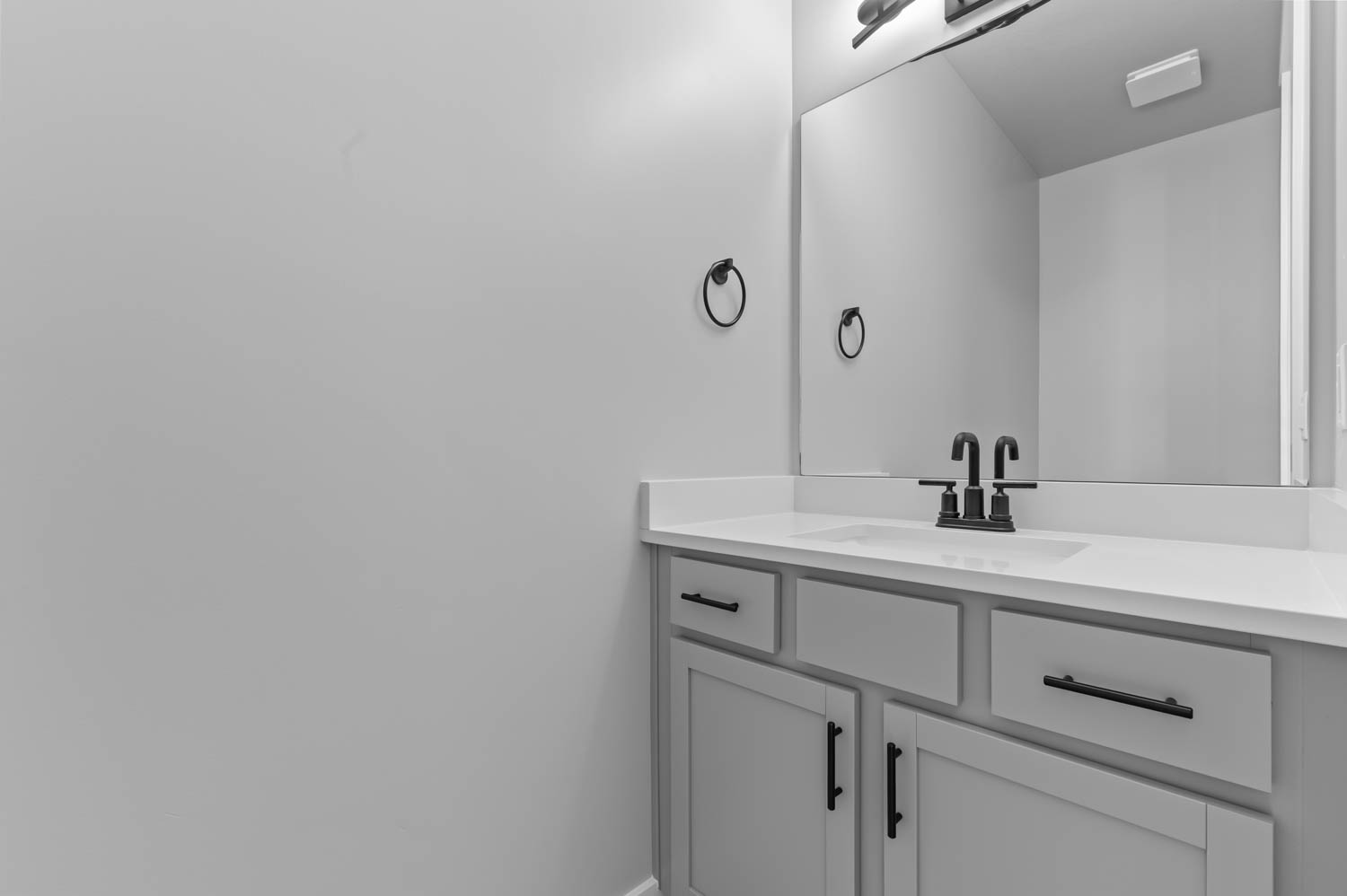 Bathroom vanity featuring light-toned cabinetry with black hardware, a white countertop, and an integrated rectangular sink