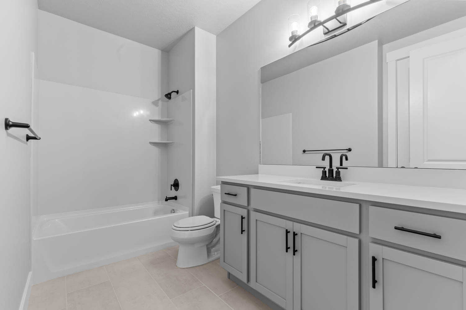 Full bathroom featuring a white tub/shower combination with integrated shelving, a single vanity with a white countertop, and light gray cabinetry with matte black hardware