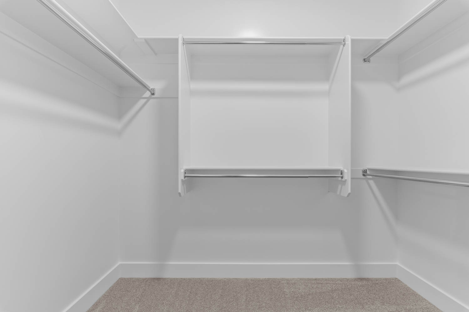 Walk-in closet featuring white built-in shelving, multiple chrome hanging rods, and light-toned carpeting