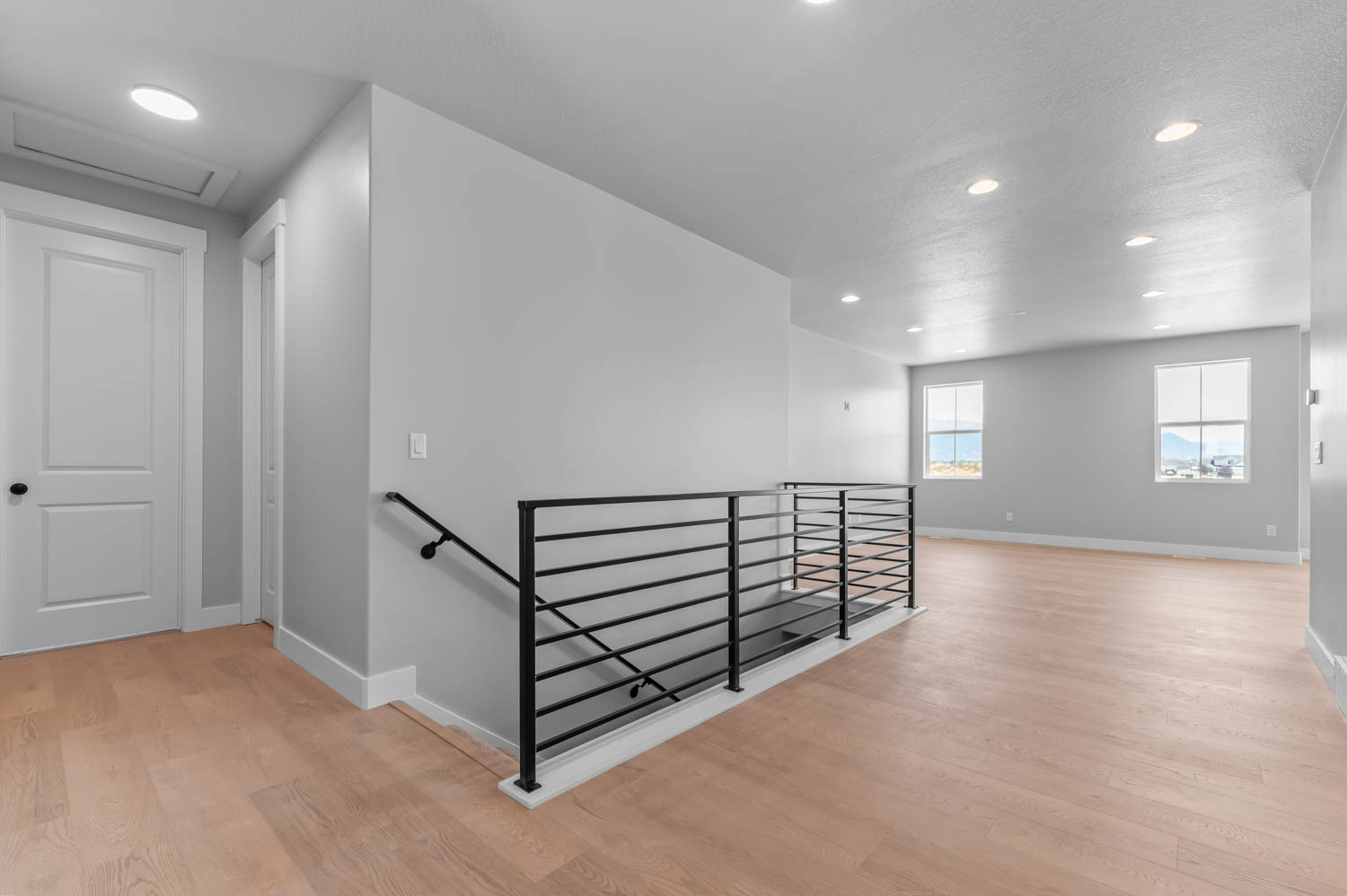 Upper-level landing featuring wood-finish flooring, recessed lighting, and a modern horizontal bar railing system