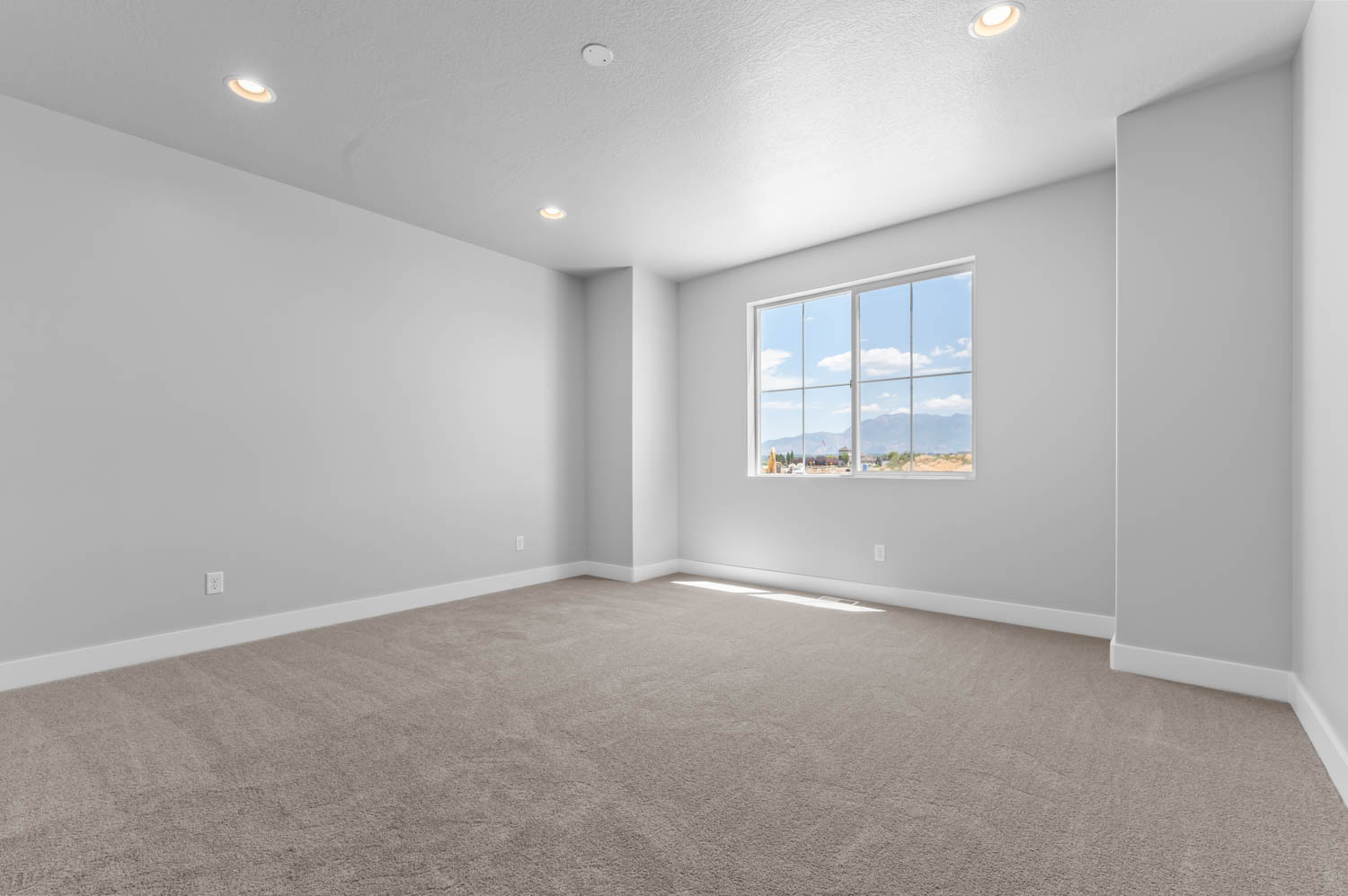 Spacious room featuring neutral carpet flooring, light gray walls, recessed ceiling lighting, and a large multi-pane window