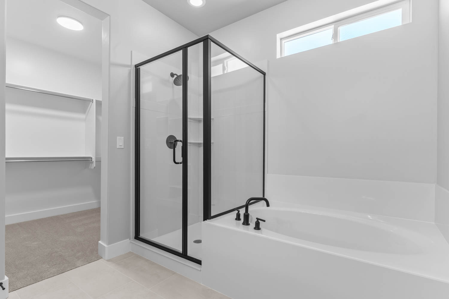 Bathroom featuring a glass-enclosed shower with matte black fixtures, an adjacent built-in soaking tub with matte black faucet, and a high transom window