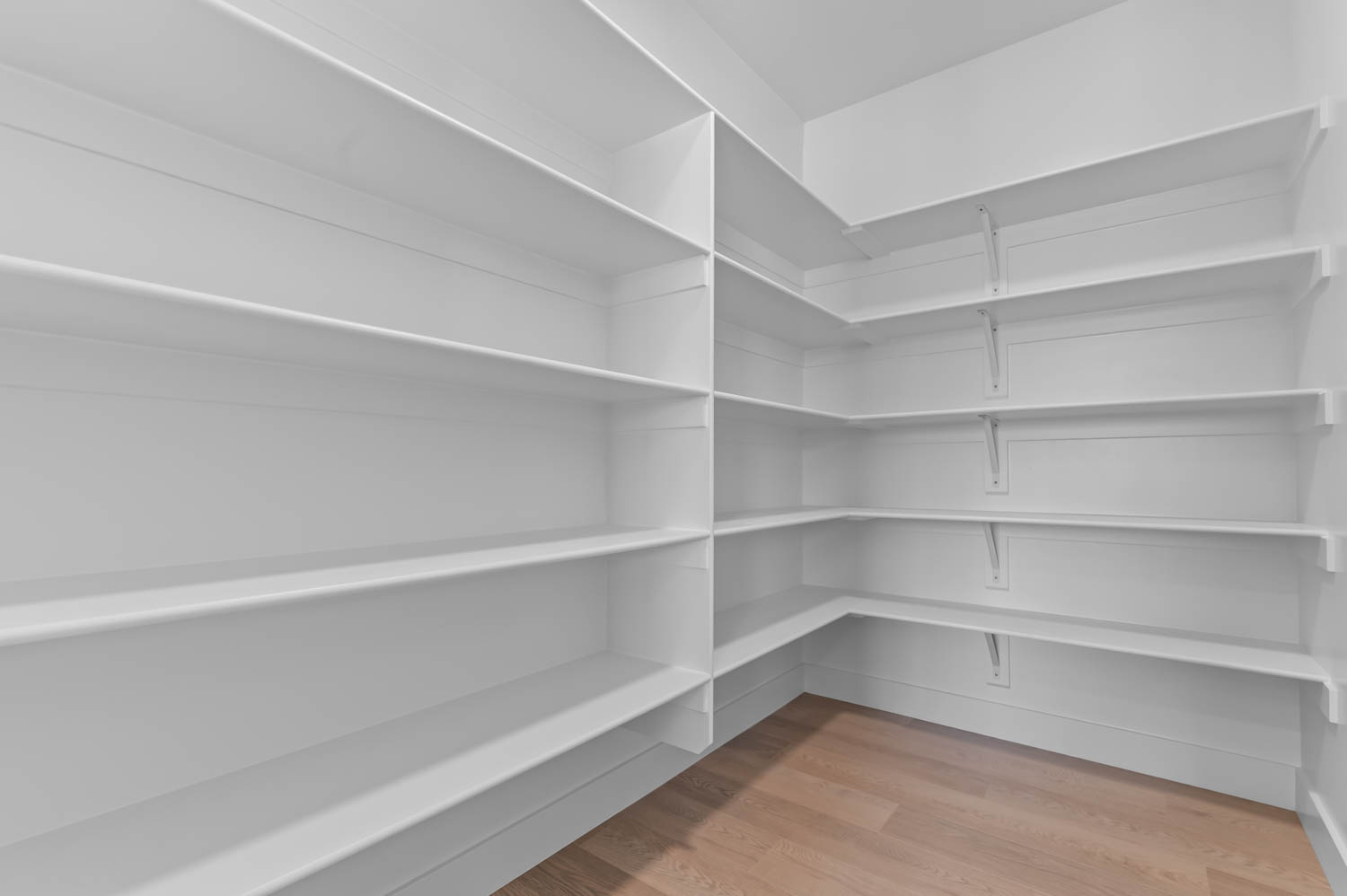 Bright white pantry featuring extensive built-in shelving, corner shelving units, and wood-finish flooring