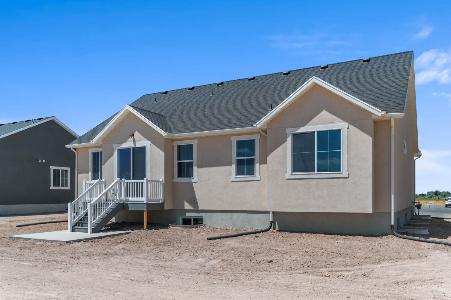 Rear exterior featuring a neutral stucco finish, white trim, and a dark shingle roof