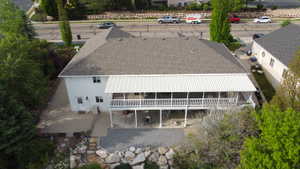 Two-story property featuring a large upper-level covered deck with white railing, a lower-level patio, and a shingle roof