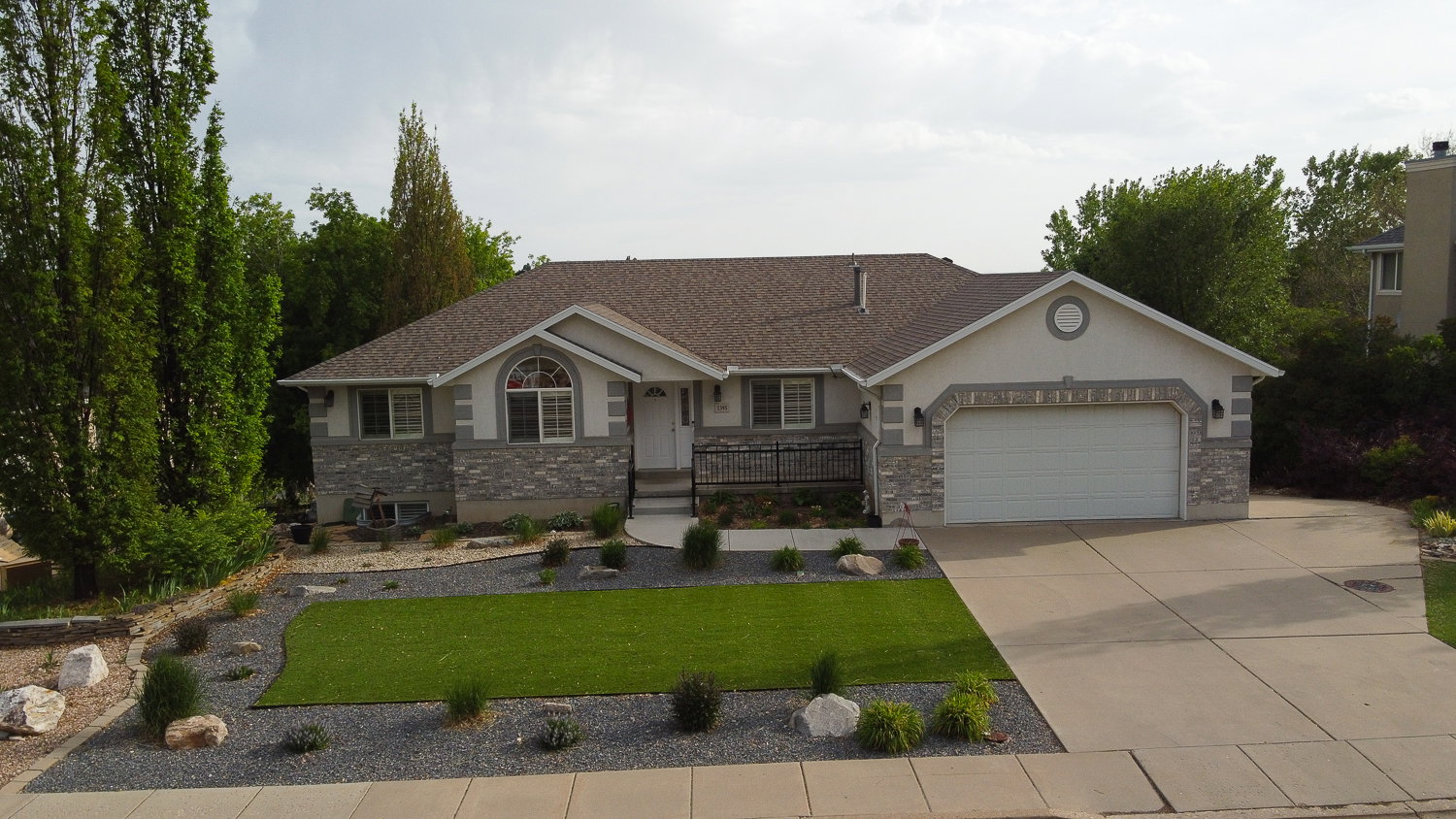 Ranch-style residence featuring a stone and stucco facade, a two-car garage, and an arched transom window above the main entry