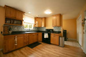 Spacious kitchen featuring warm wood cabinetry, dark countertops, a mosaic tile backsplash, and wood-finish flooring