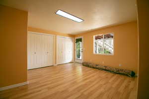 Potential downstairs bathroom. Spacious room featuring light wood-finish flooring, two sets of white bi-fold closet doors, and a rectangular ceiling light fixture