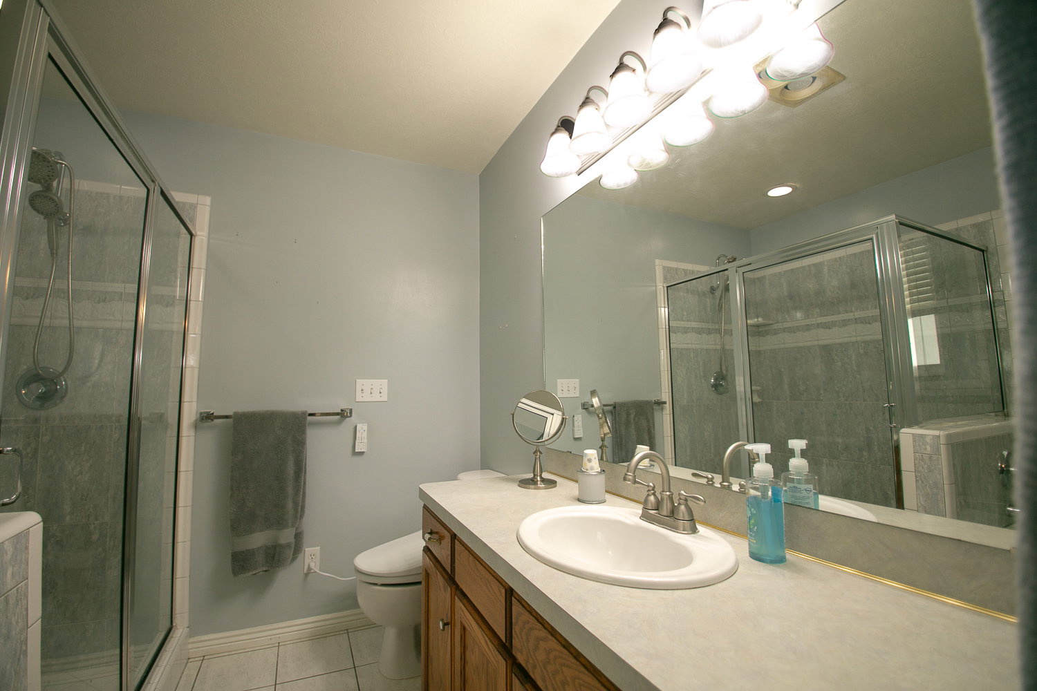 Bathroom featuring a large mirror, a vanity with wood-finish cabinetry, a built-in sink, and a glass-enclosed shower with tiled walls