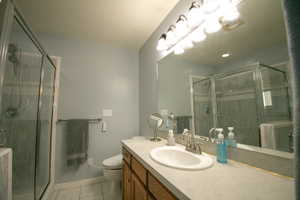 Bathroom featuring a large mirror, a vanity with wood-finish cabinetry, a built-in sink, and a glass-enclosed shower with tiled walls