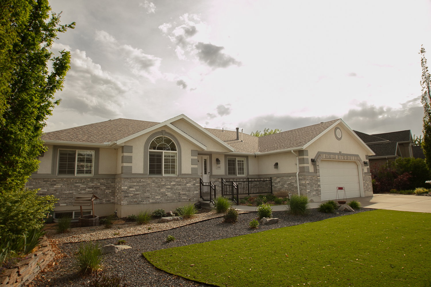 Stone and stucco facade home featuring an arched window, a two-car garage, and a sloped roofline