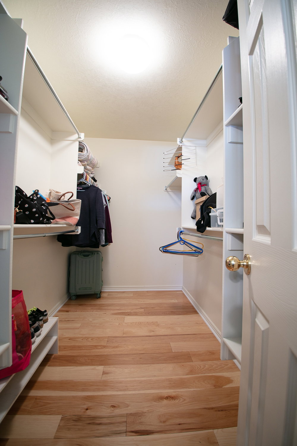 Walk-in closet featuring light wood-finish flooring, white built-in shelving, hanging rods, and a ceiling-mounted light fixture