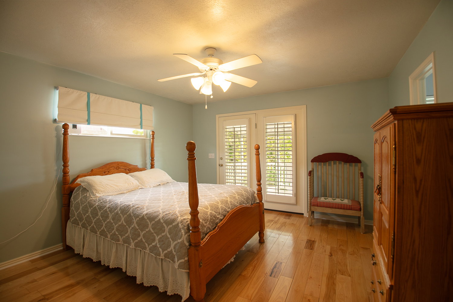 Bedroom featuring natural wood-finish flooring, light blue wall paint, and a ceiling fan with integrated lighting