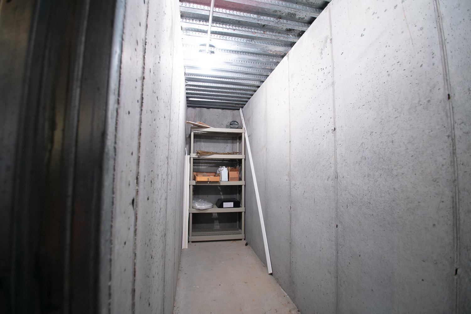 Unfinished basement utility space featuring concrete walls, a corrugated metal ceiling, and a built-in shelving unit