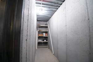 Unfinished basement utility space featuring concrete walls, a corrugated metal ceiling, and a built-in shelving unit
