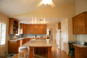 Kitchen featuring a large central island with a light-toned countertop, extensive wood cabinetry, light wood-finish flooring, recessed lighting, and a tile backsplash