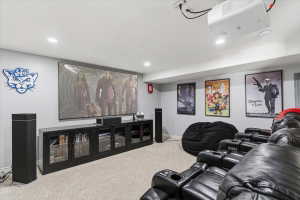 Dedicated media room featuring a large projection screen, mounted projector, recessed lighting, and light-colored carpeting