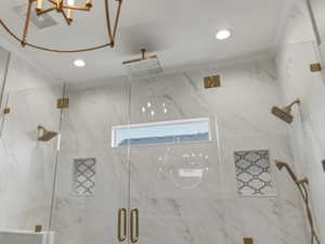 Spacious shower enclosure featuring full-height marble-look tile, frameless glass panels with brass-finish hardware, and a built-in bench