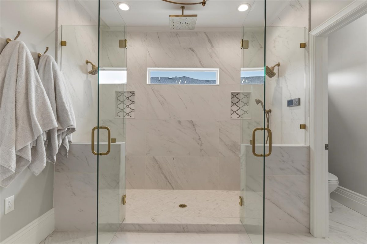 Dual-entry glass shower enclosure featuring marble-finish tile, recessed lighting, and brass-tone fixtures