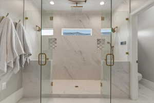 Dual-entry glass shower enclosure featuring marble-finish tile, recessed lighting, and brass-tone fixtures