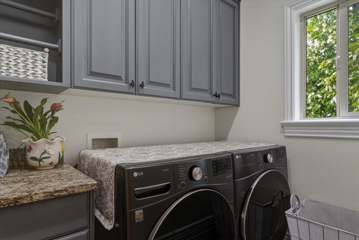 Laundry room featuring gray shaker-style cabinetry, a built-in hanging rod, a granite-look countertop, and a window with white trim