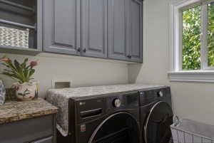 Laundry room featuring gray shaker-style cabinetry, a built-in hanging rod, a granite-look countertop, and a window with white trim