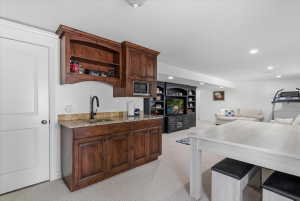 Built-in wet bar featuring wood cabinetry, granite countertop, undermount sink, and integrated microwave