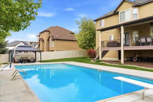 Backyard featuring a rectangular in-ground swimming pool with a diving board, surrounded by concrete decking, a gazebo, and a manicured lawn