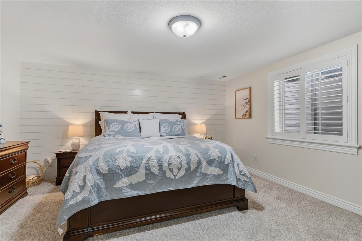 Bedroom featuring a shiplap accent wall, white plantation shutters, neutral wall paint, ceiling-mounted light fixture, and plush carpeting
