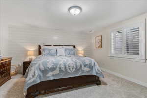 Bedroom featuring a shiplap accent wall, white plantation shutters, neutral wall paint, ceiling-mounted light fixture, and plush carpeting