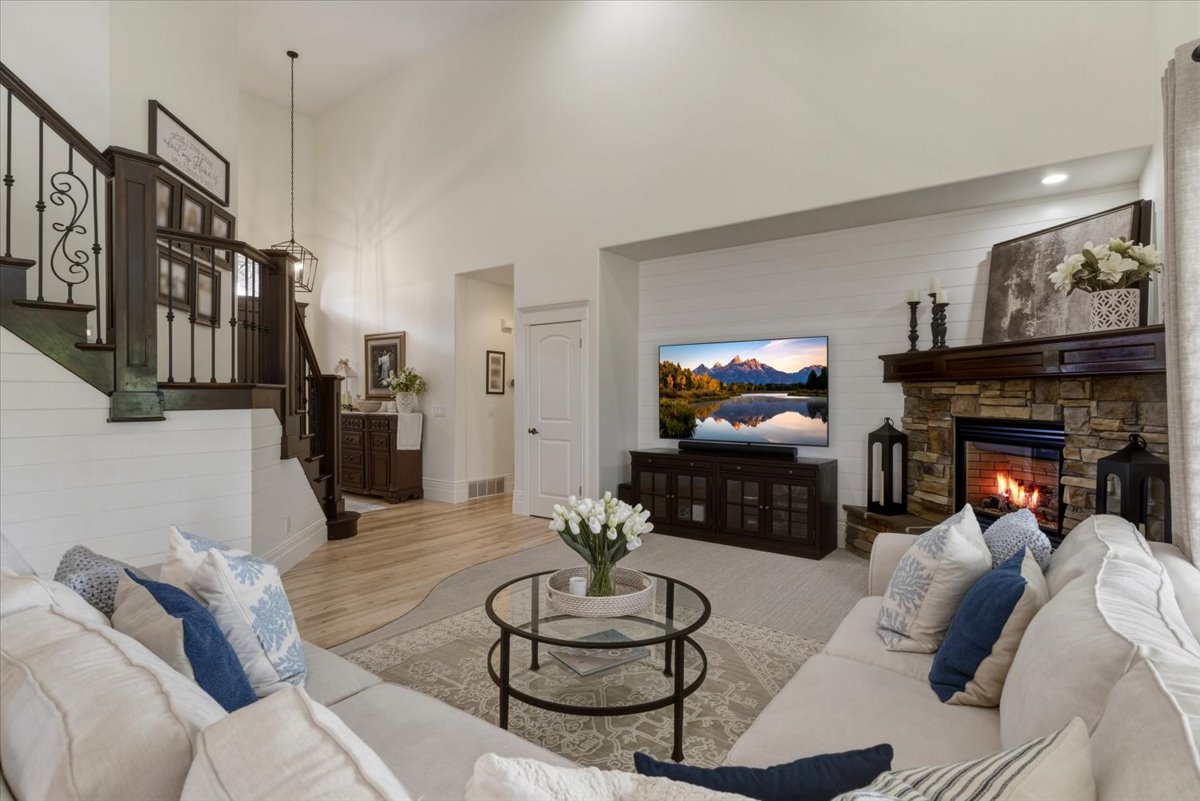 Vaulted ceiling living area featuring a stone surround fireplace with a wood mantle, shiplap accent wall, dark wood staircase with wrought iron balusters, and wood-finish flooring