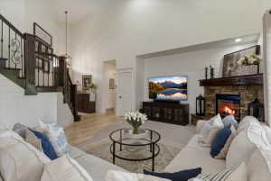 Vaulted ceiling living area featuring a stone surround fireplace with a wood mantle, shiplap accent wall, dark wood staircase with wrought iron balusters, and wood-finish flooring