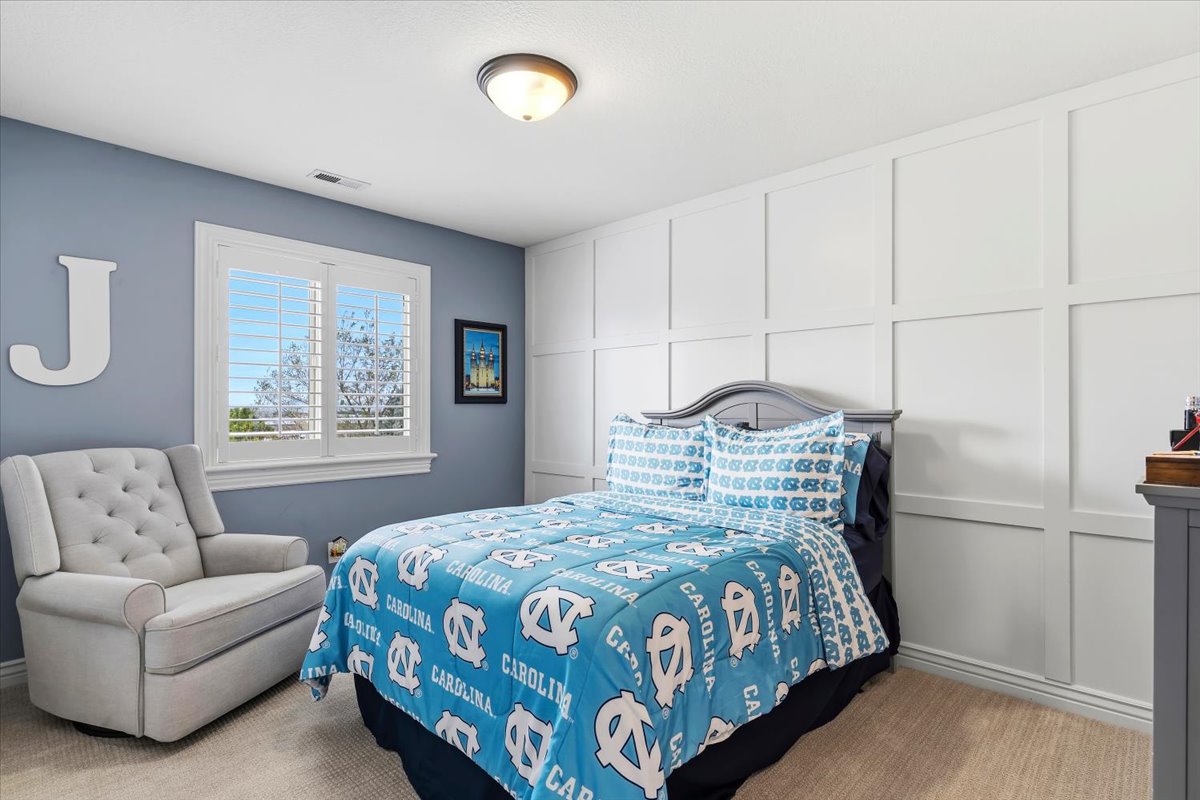 Room featuring a window with white louvered shutters, a paneled accent wall, a flush-mount ceiling light fixture, and neutral-toned carpeting