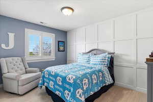 Room featuring a window with white louvered shutters, a paneled accent wall, a flush-mount ceiling light fixture, and neutral-toned carpeting