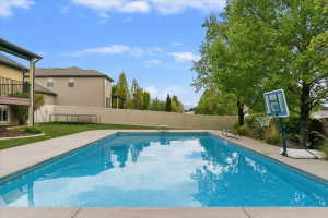 Rectangular swimming pool with concrete decking, surrounded by a manicured lawn and mature trees
