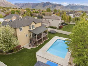 Expansive backyard featuring a rectangular swimming pool with a surrounding concrete deck, manicured lawn areas, a covered upper-level deck, and mature trees