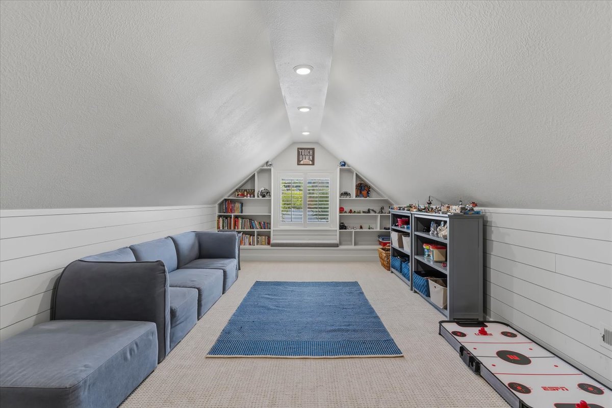 Finished attic space featuring recessed lighting, a window with plantation shutters, built-in shelving, carpet flooring, and shiplap wall detailing