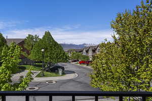 Neighborhood street featuring mature trees, residential architecture, and distant mountain scenery under a clear sky