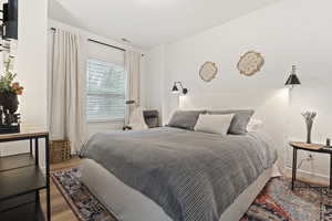 Bedroom featuring wood-finish flooring, a window with horizontal blinds and drapes, and built-in wall sconces flanking the bed