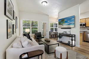 Living area with vaulted ceiling, wood-finish flooring, abundant natural light from multiple windows, and a dedicated dining space