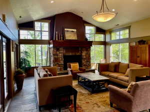 Spacious living area featuring a floor-to-ceiling stone fireplace with a wood mantel, high vaulted ceilings, expansive windows, and slate tile flooring