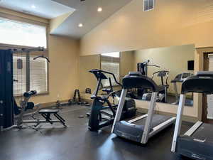 Dedicated fitness space featuring a vaulted ceiling with recessed lighting, large pane windows with horizontal blinds, full-wall mirrors, and rubber flooring